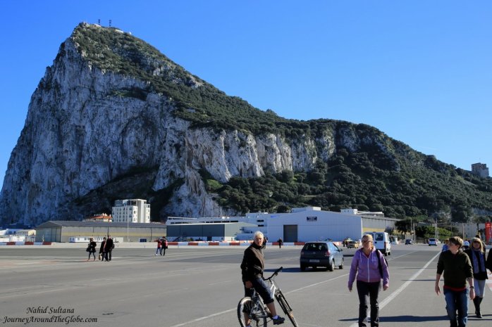 People crossing runway of Gibraltar Airport in front of The Rock (big hill in the back) in Gibraltar